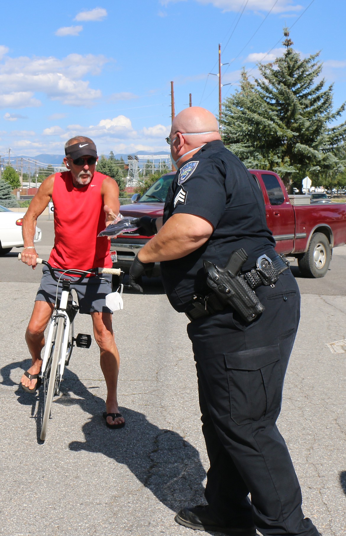 Sandpoint Police Sgt. Mike Hutter presents a bicyclist with a pack of masks during the city of Sandpoint’s second mask giveaway on Friday.