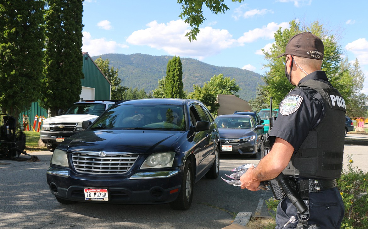 (Photo by CAROLINE LOBSINGER) 
 A Sandpoint Police officer waits as area residents driver up during the city of Sandpoint’s second mask giveaway on Friday afternoon.