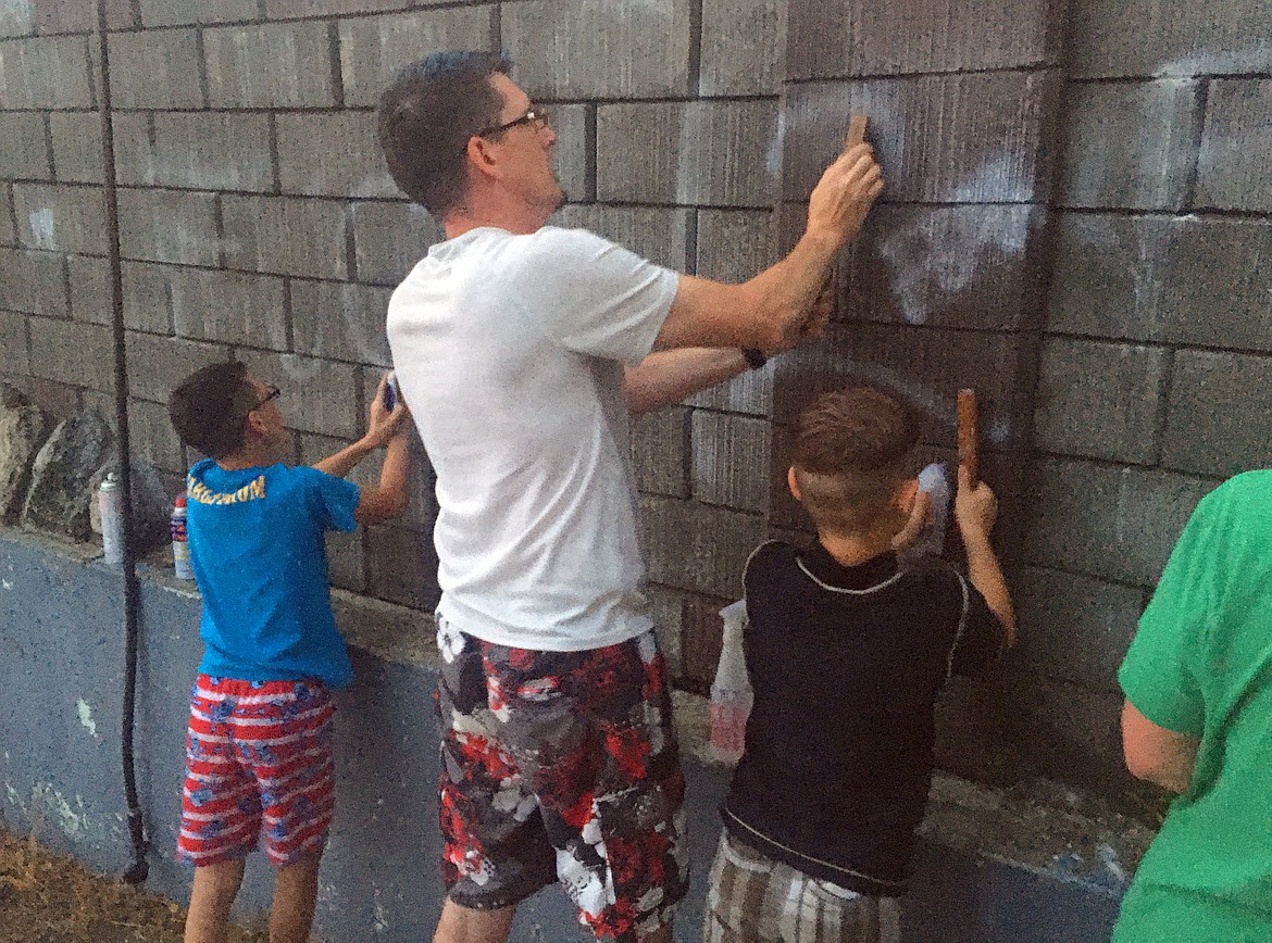 Joshua Dahlstrom is joined by sons Meshach and Kyden, right, as they scrub the wall at Sanders Beach Tuesday to remove graffiti.