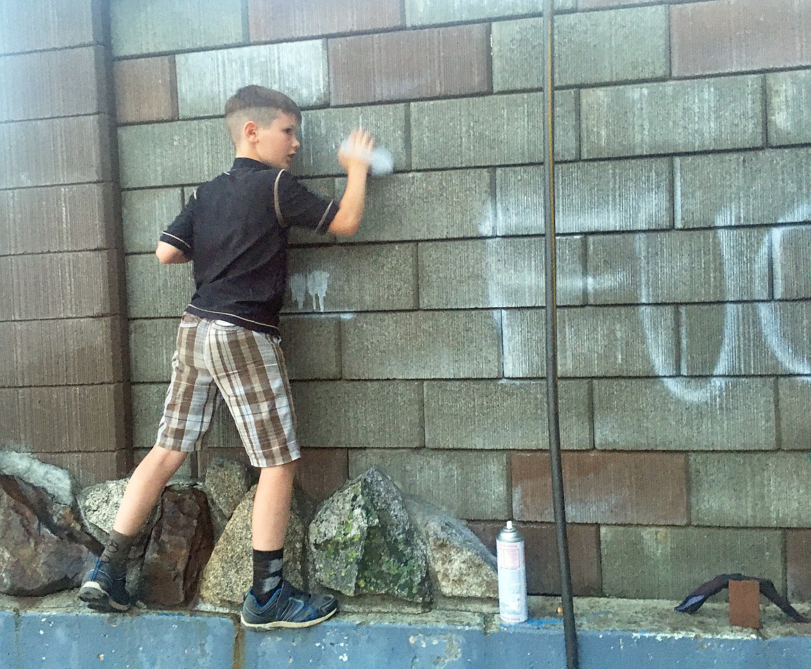 BILL BULEY/Press 
 Kydan Dahlstrom scrubs graffiti from the wall at Sanders Beach on Tuesday evening.