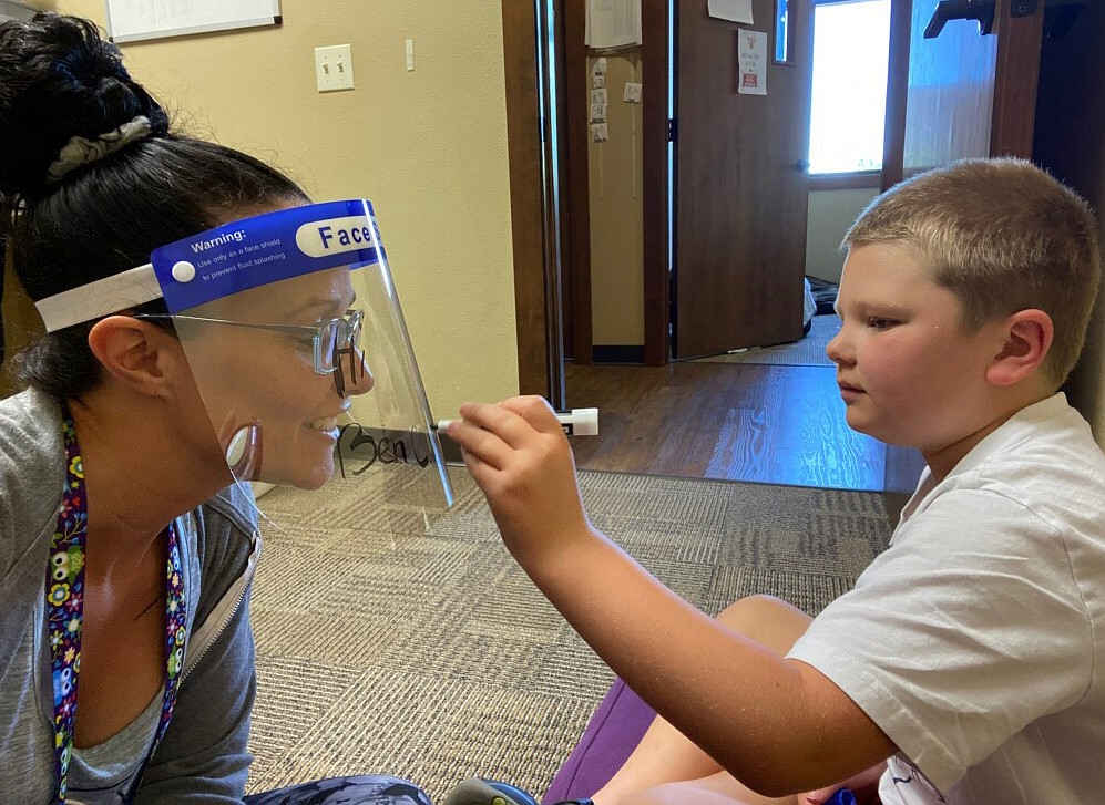 Syringa Family Partnership therapist Amy Sheppard works with Ben Christensen,7, who is having some fun with masks to get comfortable with them in July. The families Syringa serves sang the praises of the business and its loving employees, and two moms decorated the building for workers to know how much they are appreciated. (Courtesy photos)