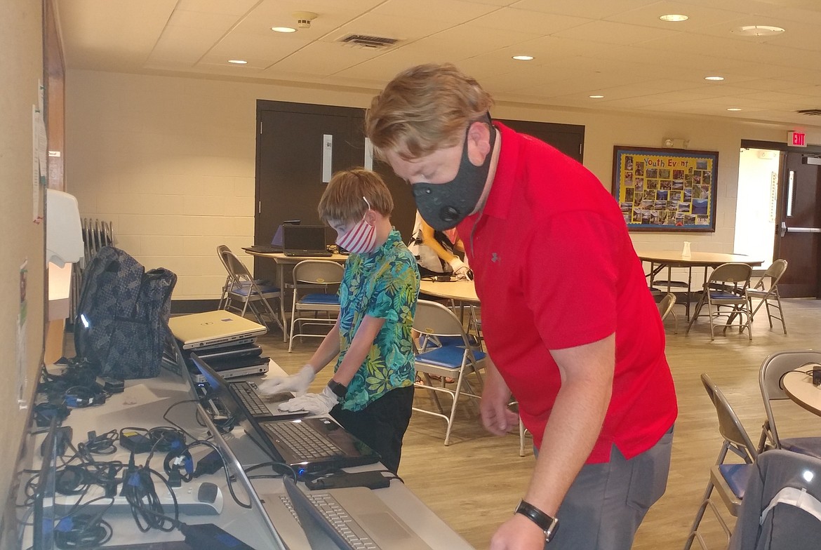 Peter Riggs and his son, Axel, wipe data and prepare devices for other volunteers to sanitize on Wednesday prior to distribution during Close the Divide Day.