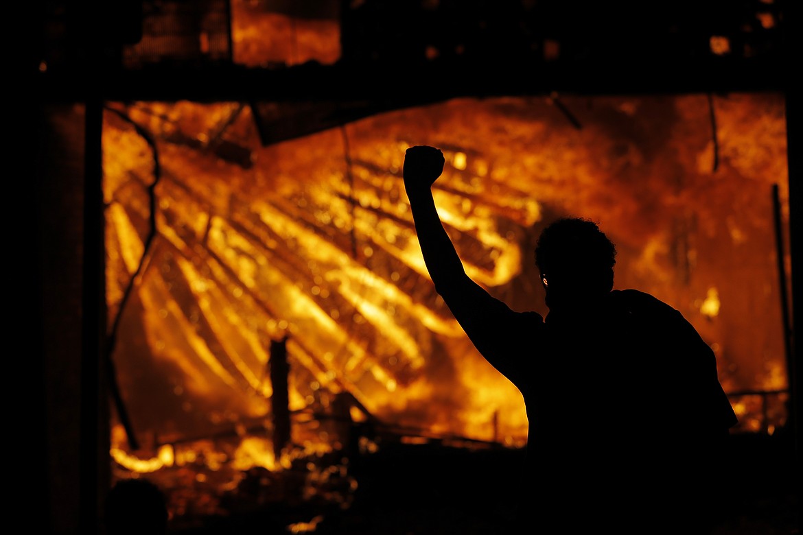 A protester gestures in front of the burning 3rd Precinct building of the Minneapolis Police Department on Thursday, May 28, 2020, in Minneapolis. Protests over the death of George Floyd, a black man who died in police custody Monday, broke out in Minneapolis for a third straight night. (AP Photo/Julio Cortez)