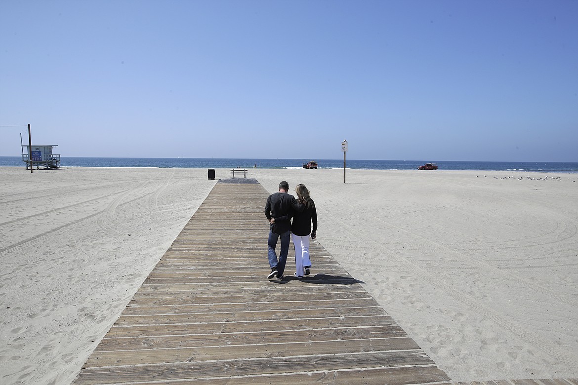 A couple hugs as they walk down a boardwalk on a mostly deserted Santa Monica beach Sunday, March 29, 2020, in Los Angeles. With cases of coronavirus surging and the death toll increasing, lawmakers are pleading with cooped-up Californians to spend a second weekend at home to slow the spread of the infections. (AP Photo/Marcio Jose Sanchez)
