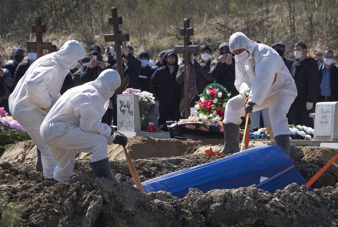 Grave diggers wearing protective suits bury a COVID-19 victim as relatives and friends stand at a safe distance, in the special purpose for coronavirus victims section of a cemetery in Kolpino, outside St.Petersburg, Russia, Sunday, May 10, 2020. (AP Photo/Dmitri Lovetsky)