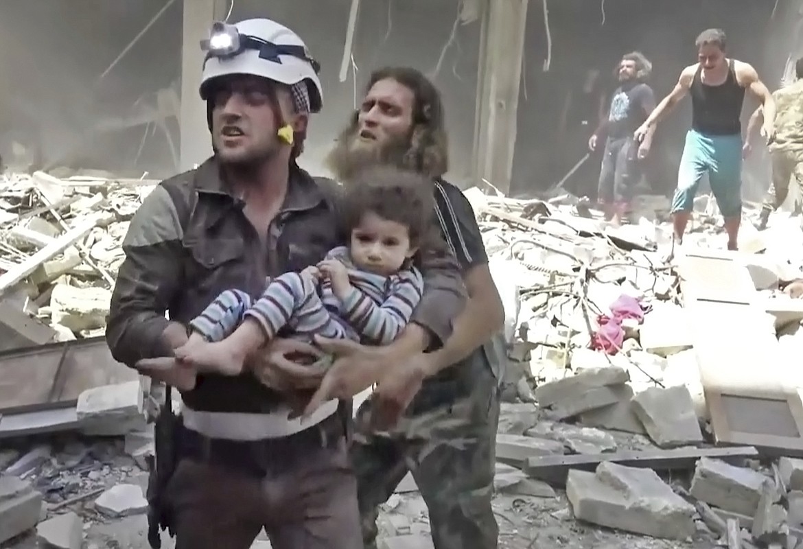 FILE - In this image made from video and posted online by Validated UGC on Thursday, April 28, 2016, a civil defense worker carries a child after airstrikes hit Aleppo, Syria. In 2016, repeated cease-fire negotiations failed to halt relentless warfare among multiple factions. With Russia's help, the government forces of President Bashar Assad finally seized rebel-held portions of the city of Aleppo, at a huge cost in terms of deaths and destruction. (Validated UGC via AP video)