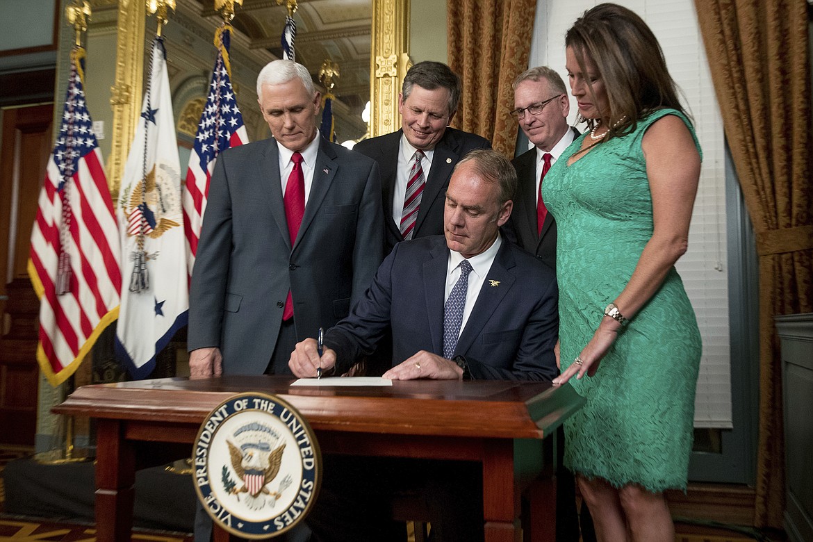 FILE - In this March 1, 2017 file photo, Vice President Mike Pence, left, Sen. Steve Daines, R-Mont., second from left, Montana Attorney General Tim Fox, second from right, and Lolita Hand, right, watches as Interior Secretary Ryan Zinke signs an official document in the Eisenhower Executive Office Building on the White House complex in Washington. Lolita Hand is Zinke's wife. Zinke was the Republican Party's first choice to take on incumbent Democratic Sen. Jon Tester in 2018, but President Donald Trump dashed those hopes by snatching the former congressman to become his interior secretary. Now the Republicans in Montana and in Washington, D.C., are now courting Fox to step up and run against Tester. (AP Photo/Andrew Harnik, File)