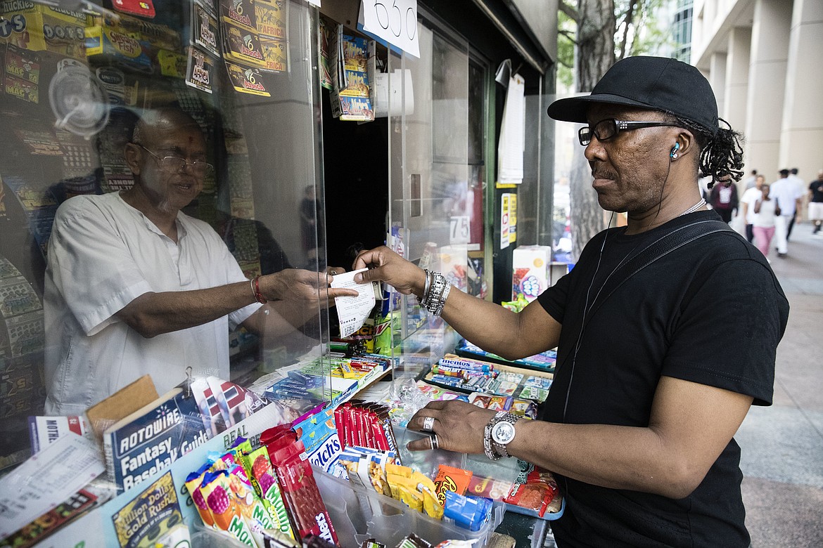 Atul Amin, left, sells a customer a Powerball ticket at his news stand in Philadelphia, Tuesday, Aug. 22, 2017. The Powerball jackpot has climbed to $700 million, giving players a chance to dream of winning the second-largest lottery prize in U.S. history. (AP Photo/Matt Rourke)