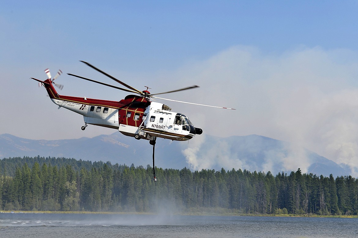 In an Aug. 30, 2017 photo, a helicopter crew fills up the water tank on their chopper in Seeley Lake, Mont., as they help battle the Rice Ridge Fire which continues to threaten the town of Seeley Lake. The air quality in Seeley Lake had hourly pollution readings classified as hazardous in 26 days in August. (Rion Sanders/The Great Falls Tribune via AP)