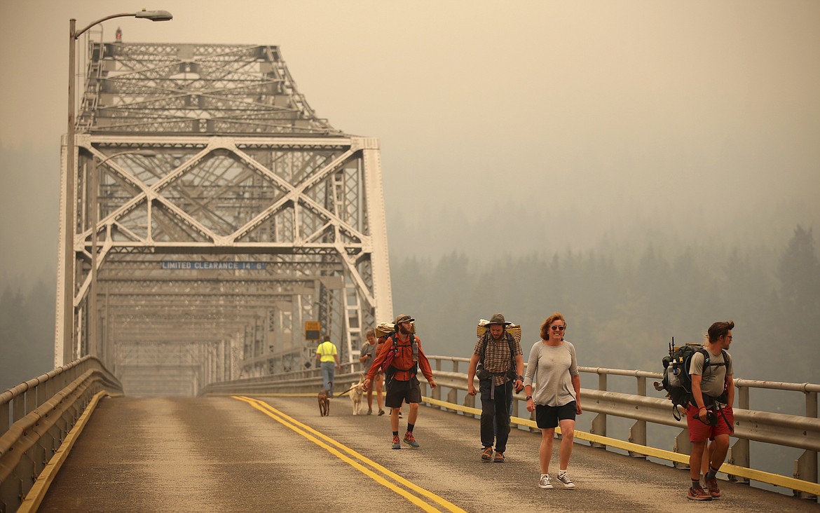 Pedestrians walk off the Bridge of the Gods, which spans the Columbia River between Washington and Oregon states, as smoke from the Eagle Creek wildfire obscures the Oregon hills in the background near Stevenson, Wash., Wednesday, Sept. 6, 2017. The Eagle Creek fire continues to burn on the Oregon side of the river near the town of Cascade Locks, Ore. Officials closed the bridge to pedestrians and onlookers after this photo was taken. (AP Photo/Randy L. Rasmussen)