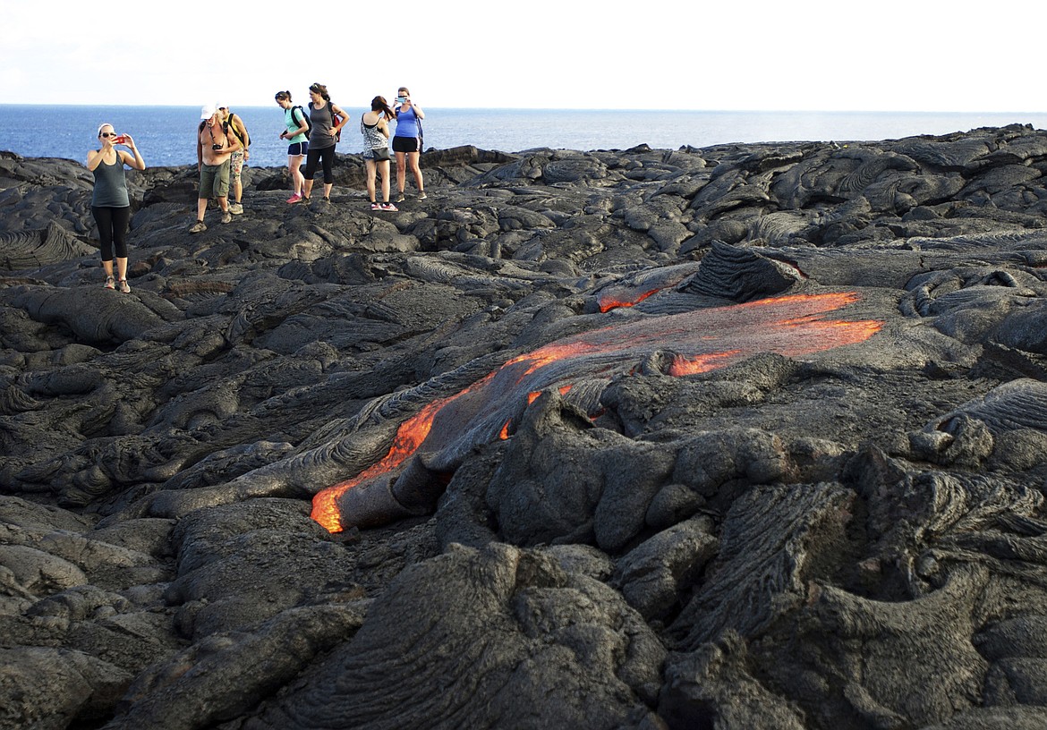 FILE - In this Monday, Aug. 8, 2016 file photo, visitors look at lava from Kilauea, an active volcano on Hawaii&#146;s Big Island, as it flows toward the ocean in Hawaii Volcanoes National Park near Kalapana, Hawaii. Hawaii residents and an organization representing federal workers filed a lawsuit against the Federal Aviation Administration on Wednesday, Oct. 4, 2017 seeking to force it to do something about tour helicopters buzzing their communities and national parks across the country.  (AP Photo/Caleb Jones, File)