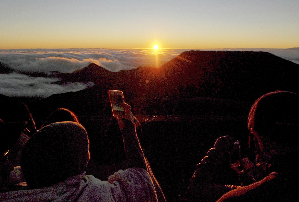 FILE - In this Jan. 22, 2017 file photo, people watch as the sun rises in front of the summit of Haleakala volcano in Haleakala National Park on Hawaii&#146;s island of Maui. Hawaii residents and an organization representing federal workers filed a lawsuit against the Federal Aviation Administration on Wednesday, Oct. 4, 2017 seeking to force it to do something about tour helicopters buzzing around seven national parks across the country.  (AP Photo/Caleb Jones, File)