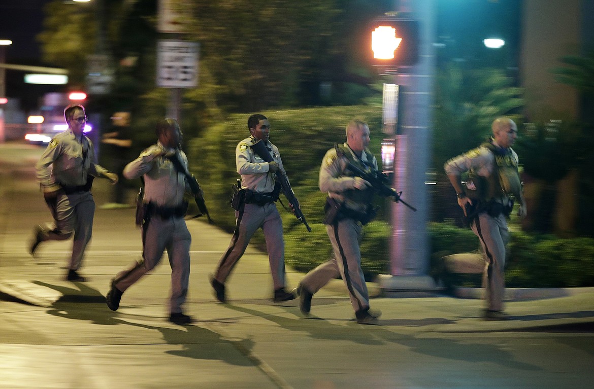 Police run to cover at the scene of a shooting near the Mandalay Bay resort and casino on the Las Vegas Strip, Sunday, Oct. 1, 2017, in Las Vegas. Multiple victims were being transported to hospitals after a shooting late Sunday at a music festival on the Las Vegas Strip. (AP Photo/John Locher)