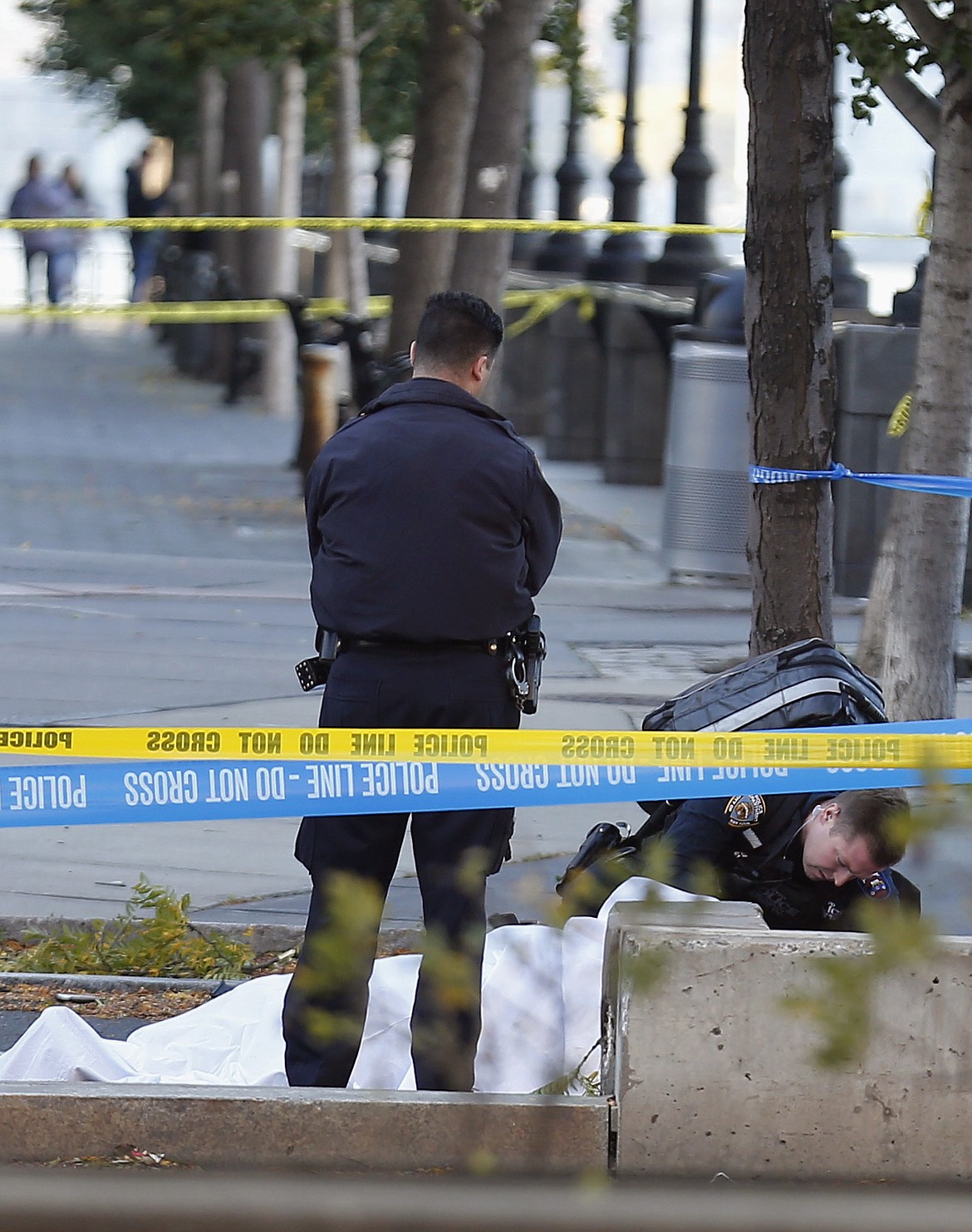 A paramedic looks at a body covered under a white sheet along the bike path Tuesday Oct. 31, 2017, in New York. (AP Photo/Bebeto Matthews)