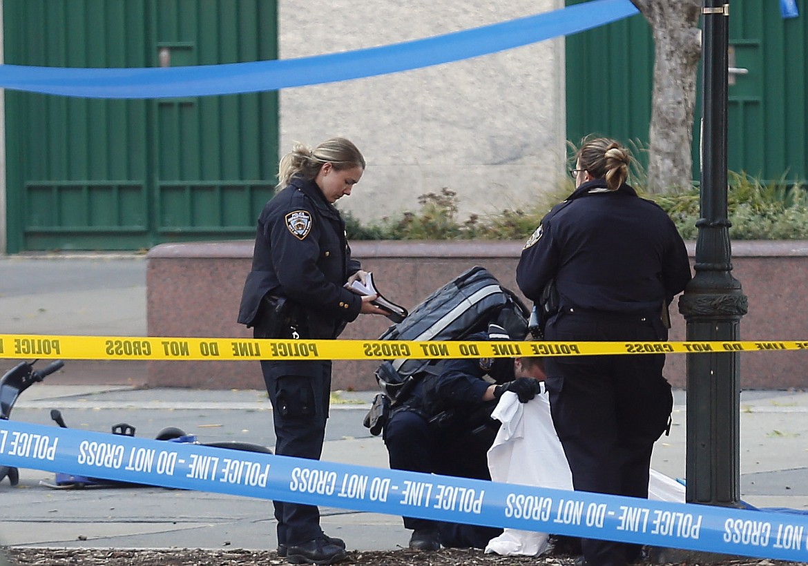 A paramedic looks at a body covered under a white sheet along a bike path, Tuesday Oct. 31, 2017, in New York. (AP Photo/Bebeto Matthews)