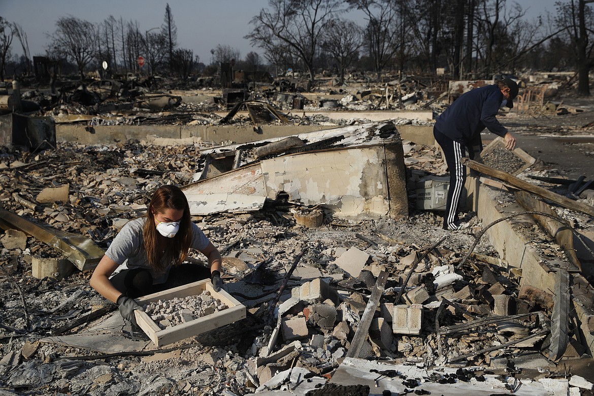 FILE - In this Oct. 15, 2017, file photo, Ed Curzon, right, and his daughter Margaret sift debris to salvage anything they can from the rubble of their home, destroyed by a wildfire in the Coffey Park neighborhood in Santa Rosa, Calif. If House Republicans have their way, victims of hurricanes in Texas and Florida could deduct their losses on their taxes. But victims of the California wildfires no longer could. (AP Photo/Jae C. Hong, File)