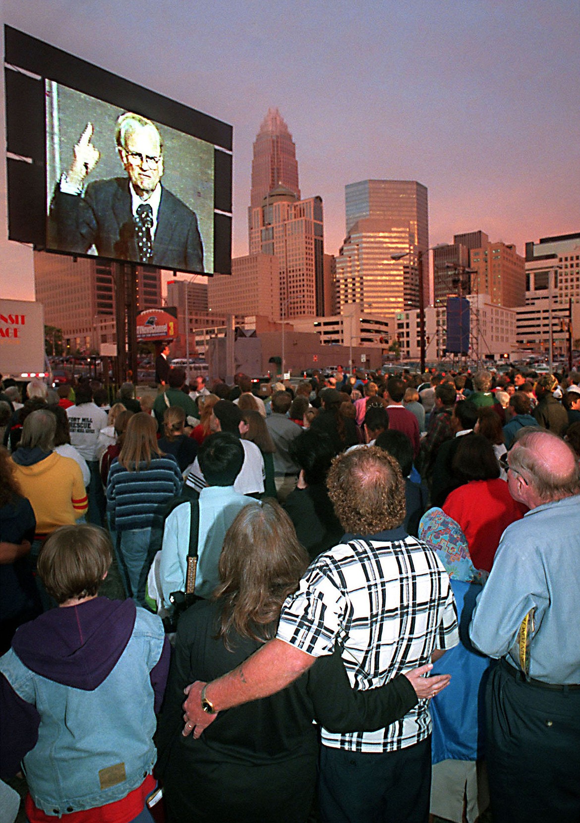 In an overflow area on Mint Street, from left, Paula and William Childres stand with their arms around each other and listen to the Rev. Billy Graham on the big screen during a September 29, 1996 event. (Diedra Laird/Charlotte Observer/TNS)