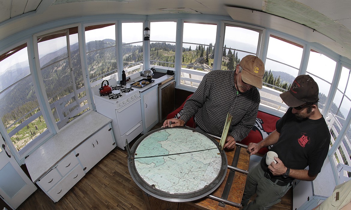 In this Wednesday, July 18, 2018, photo, Tom VandeWater, left, explains how he uses a device called the Osborne Fire-Finder to pinpoint the location of any smoke or fires he spots from the Coolwater Fire Lookout to Cory Guffey, a U.S. Forest Service initial attack crew captain, at the Coolwater Fire Lookout in the Nez Perce-Clearwater National Forests near Lowell, Idaho. (AP Photo/Ted S. Warren)