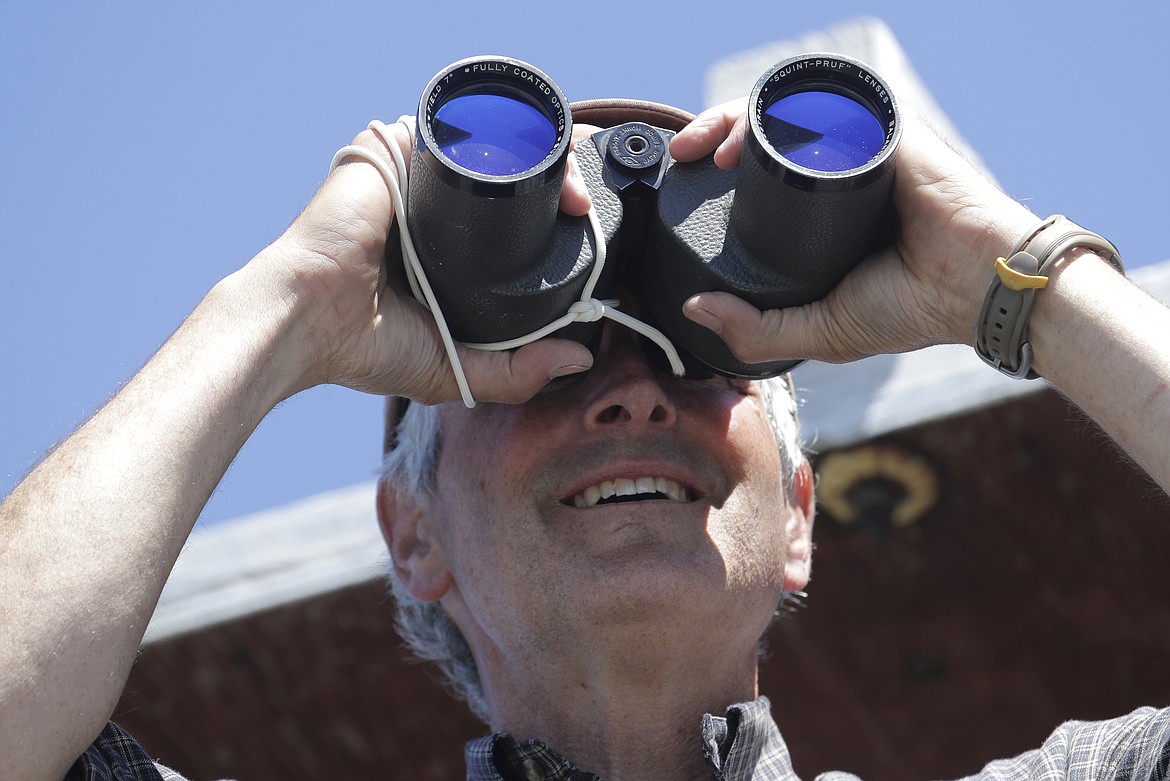 In this Wednesday, July 18, 2018, photo, Tom VandeWater stands at the railing of the Coolwater Fire Lookout and looks through his binoculars in the Nez Perce-Clearwater National Forests near Lowell, Idaho. VandeWater, from Canton, N.Y., has staffed the lookout each summer for many years for the U.S. Forest Service. (AP Photo/Ted S. Warren)