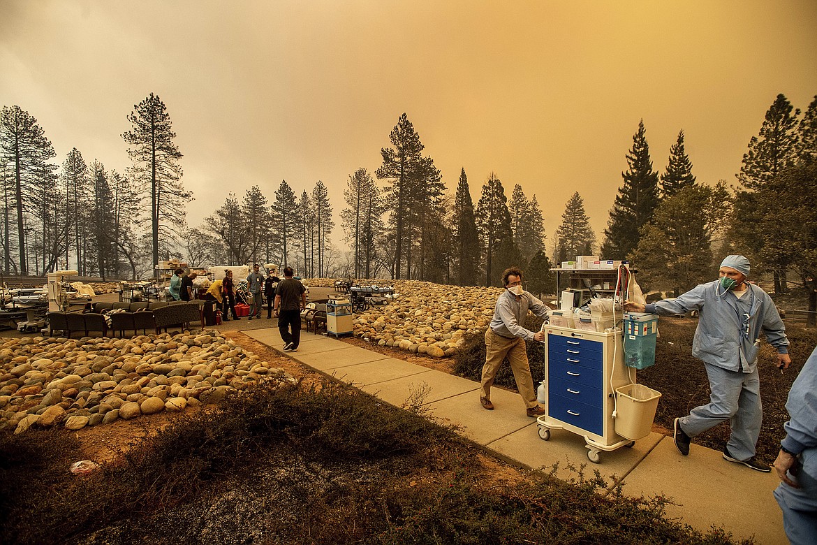 Medical workers move equipment from a makeshift emergency room while the Feather River Hospital burns as the Camp Fire rages through Paradise, Calif., on Thursday, Nov. 8, 2018. Tens of thousands of people fled a fast-moving wildfire Thursday in Northern California, some clutching babies and pets as they abandoned vehicles and struck out on foot ahead of the flames that forced the evacuation of an entire town. (AP Photo/Noah Berger)