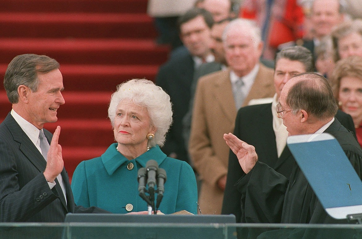 FILE - In this Jan. 20, 1989, file photo, President George H.W. Bush raises his right hand as he is sworn into office as the 41st president of the United States by Chief Justice William Rehnquist outside the west front of the Capitol as first lady Barbara Bush holds the bible for her husband. Bush died at the age of 94 on Friday, Nov. 30, 2018, about eight months after the death of his wife, Barbara Bush. (AP Photo/Bob Daugherty, File)