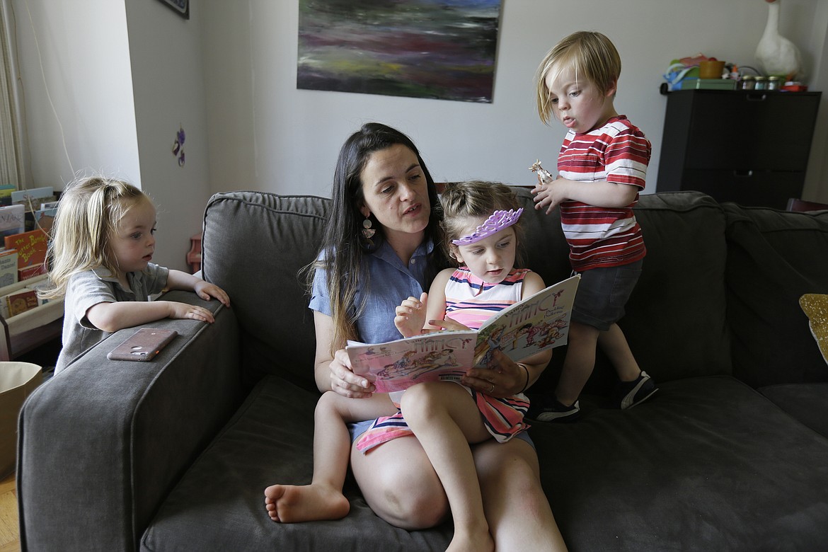 In this Thursday, June 6, 2019 photo, Sarah Montoya reads to her daughter, Walden, as her twins Nicasio, left, and Farallon, right, look on at their home in San Francisco. During last year's deadly Camp Fire, which killed 85 people and destroyed 14,000 homes, smoke from the blaze inundated a San Francisco neighborhood roughly 170 miles away where Montoya lives with her husband, Trevor McNeil, and their three children. All three children have respiratory problems suspected to be asthma. But when the smoke from the Camp Fire filled the air for two weeks, the family was unable to find child-sized face masks to protect them or an air filter to clear the air in their house. (AP Photo/Eric Risberg)