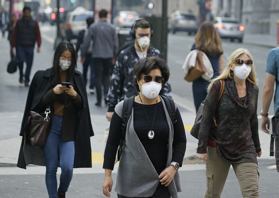 In this 2018 file photo, people wear masks while walking through the Financial District in the smoke-filled air in San Francisco. Tens of millions of people in the Western US face a growing health risk due to wildfires as more intense and frequent blazes churn out greater volumes of lung-damaging smoke, according to research scientists at NASA and several major universities. (AP Photo/Eric Risberg, File)