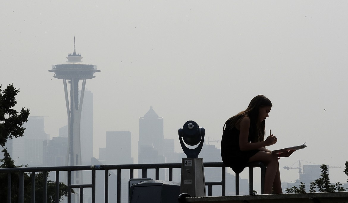 FILE - In this Aug. 14, 2018 file photo, a girl works on a drawing next to an unused viewing scope as a smoky haze obscures the Space Needle and downtown Seattle behind. Tens of millions of people in the Western US face a growing health risk due to wildfires as more intense and frequent blazes churn out greater volumes of lung-damaging smoke, according to research scientists at NASA and several major universities. (AP Photo/Elaine Thompson, File)