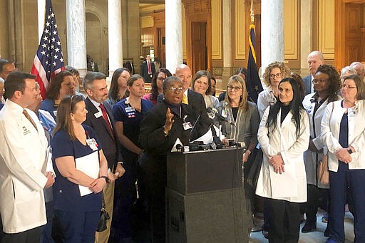 Denise Dillard, chief of advocacy for Methodist Hospitals in Gary and Merrillville, is surrounded by doctors and nurses from around Indiana as she speaks during a news conference Monday, March 2, 2020, at the Statehouse in Indianapolis. Dillard and others argue that a legislative proposal limiting how much hospitals could charge for procedures done at non-hospital facilities could lead to widespread medical service cuts. (AP Photo/Tom Davies)