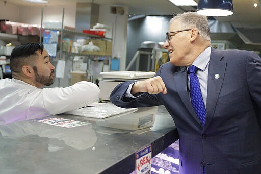 Washington Gov. Jay Inslee, right, bumps elbows with a worker at the seafood counter of the Uwajimaya Asian Food and Gift Market, Tuesday, March 3, 2020, in Seattle's International District. Inslee said he's doing the elbow bump with people instead of shaking hands to prevent the spread of germs, and that his visit to the store was to encourage people to keep patronizing businesses during the COVID-19 Coronavirus outbreak. Earlier in the day, following a tour at a health clinic, Inslee urged people to wash hands frequently and practice other measures of health hygiene, and to stay home from work and public events if they don't feel well or have any symptoms of illness. (AP Photo/Ted S. Warren)