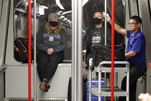 Travelers Meredith Ponder, left, and Coleby Hanisch, both of Des Moines, Iowa, wear masks to remind them not to touch their faces as they ride a train at Seattle-Tacoma International Airport Tuesday, March 3, 2020, in SeaTac, Wash. Six of the 18 Western Washington residents with the coronavirus have died as health officials rush to test more suspected cases and communities brace for spread of the disease. All confirmed cases of the virus in Washington are in Snohomish and King counties. (AP Photo/Elaine Thompson)