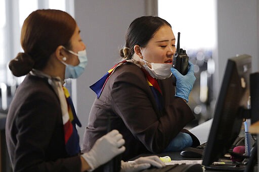 A gate agent pulls down her mask to speak on a radio at Seattle-Tacoma International Airport Tuesday, March 3, 2020, in SeaTac, Wash. Six of the 18 Western Washington residents with the coronavirus have died as health officials rush to test more suspected cases and communities brace for spread of the disease. All confirmed cases of the virus in Washington are in Snohomish and King counties. (AP Photo/Elaine Thompson)