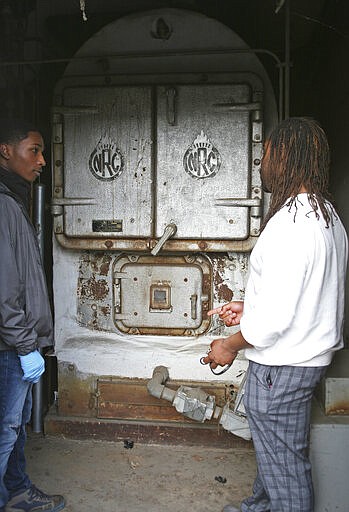 FILE - In this Monday, Jan. 27, 2020, file photo, Lake Elementary School principal Kenneth Bonner, right, and school custodian Perrione Pearson, stand in front of the school's aging furnace, wrapped in asbestos insulation and taped up with duct tape in San Pablo, Calif. Officials say the furnace may date to the school's construction in 1957. The only statewide measure on Tuesday's California primary ballot, Proposition 13, is a $15 billion bond to repair and modernize aging schools, many of which are more than a half-century old and have issues ranging from leaky roofs and old wiring to toxic mold.(AP Photo/Jocelyn Gecker, File)