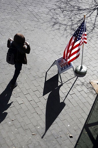 A pedestrian walks past the flag and voting place site at the downtown library in Minneapolis as part of Minnesota's Super Tuesday presidential nomination primary March 3, 2020. (AP Photo/Jim Mone)