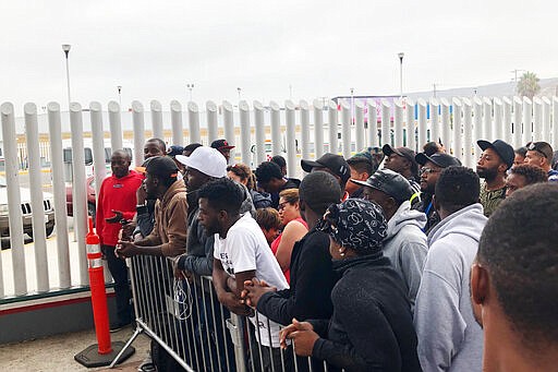 FILE - In this Sunday, July 28, 2019, file photo, migrants in Tijuana, many from Cameroon, listen to names being called for those who can claim asylum that day in the US.  President Donald Trump isn't the only world leader making it virtually impossible for many Africans to get asylum in the United States.  Ecuador is closing its doors as one of the few countries in North and South America to welcome African visitors, depriving them of a starting point for their dangerous journeys north by land. (AP Photo/Elliot Spagat, File)