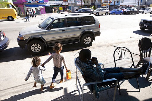 In this Feb. 7, 2020, image, an African seeking asylum sits in front of his apartment in Tijuana, Mexico, as two children pass.  Many countries in North and South America are blocking the path for Africans who are struggling to seek asylum in the United States. People from Cameroon and other African nations often win their cases in the United States but they first must reach American soil.   (AP Photo/Gregory Bull)