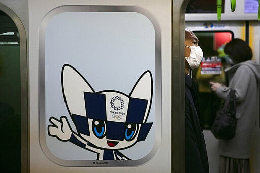 A man wearing a mask commutes in a train decorated with a poster showing Miraitowa, the official mascot of the Tokyo 2020 Olympics, Tuesday, March 3, 2020, in Tokyo. The Japanese government has indicated it sees the next couple of weeks as crucial to containing the spread of COVID-19, which began in China late last year. (AP Photo/Jae C. Hong)