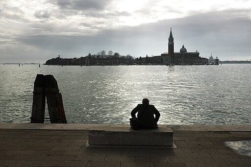 A man sits on a bench on a promenade next to the lagoon of Venice, Italy, Tuesday, March 3, 2020. G-7 countries say they are ready to take action to cushion the economic impacts of the new coronavirus outbreak, a statement that comes after a few days of wild market swings. (AP Photo/Francisco Seco)