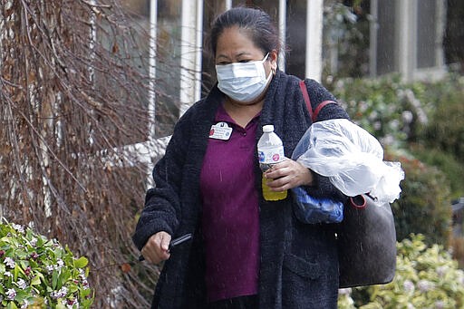 A worker wears a mask at the Life Care Center in Kirkland, Wash., near Seattle, walks near a UPS truck during a package delivery, Monday, March 2, 2020. Several of the people who have died in Washington state from the COVID-19 coronavirus were tied to the long-term care facility, where dozens of residents were sick. (AP Photo/Ted S. Warren)