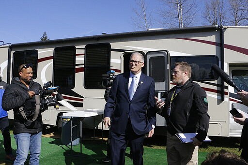 Washington Gov. Jay Inslee, center, stands in front of a recreation vehicle at a potential coronavirus isolation and quarantine site with Nathan Weed, incident commander for the coronavirus response team at Department of Health, Wednesday, March 4, 2020, in Centralia, Wash. Eight RVs are located at the site. The state has now reported 39 COVID-19 cases, all in the greater Seattle area, including 10 deaths. (AP Photo/Rachel La Corte)