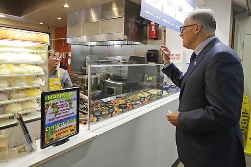 Washington Gov. Jay Inslee, right, orders food at the Uwajimaya Asian Food and Gift Market, Tuesday, March 3, 2020, in Seattle's International District. Inslee said the visit was to encourage people to keep patronizing businesses during the COVID-19 Coronavirus outbreak. Earlier in the day, following a tour at a health clinic, Inslee urged people to wash hands frequently and practice other measures of health hygiene, and to stay home from work and public events if they don't feel well or have any symptoms of illness. (AP Photo/Ted S. Warren)