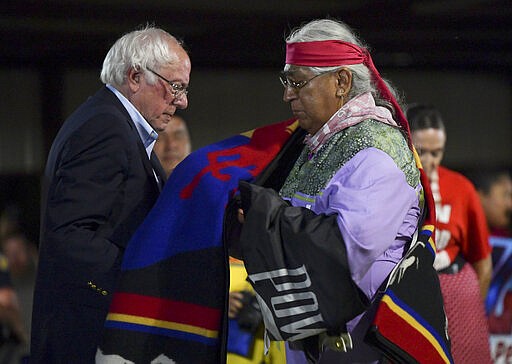 FILE - In this Sept. 22, 2019, file photo, Democratic presidential candidate U.S. Sen. Bernie Sanders receives an honor blanket from Cornel Pewewardy at the annual Comanche Nation Fair Powwow, in Lawton, Okla. Sanders hopes Super Tuesday, March, 3, 2020, in Oklahoma will be a repeat of his performance four years ago, while the rest of the Democratic field hope to get a foothold in the Sooner State as voters in 14 states head to the polls.(AP Photo/Gerardo Bello, File)