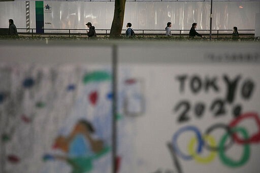 Commuters walk along a sidewalk as a poster celebrating the Tokyo 2020 Olympics is seen in foreground, Tuesday, March 3, 2020, in Tokyo. The Japanese government has indicated it sees the next couple of weeks as crucial to containing the spread of COVID-19, which began in China late last year. (AP Photo/Jae C. Hong)