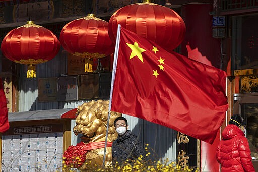 A masked man looks out near a national flag outside a traditional medicine hospital in Beijing on Tuesday, March 3, 2020. Mushrooming outbreaks in the Mideast, Europe and South Korea contrasted with optimism in China, where thousands of recovered patients were going home and new virus cases drop to a new low. (AP Photo/Ng Han Guan)