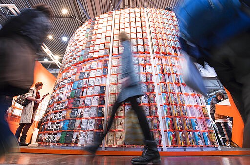 FILE --- In this Thursday, March 15, 2018 photo visitors walk past a booth in one of the exhibition halls during the opening day at the Leipzig International Book Fair in Leipzig, Germany. The Leipzig book fair 2020 which was planed to took place between March 12 and March 15, 2020 has been chancelled due to the the new coronavirus. (AP Photo/Jens Meyer)