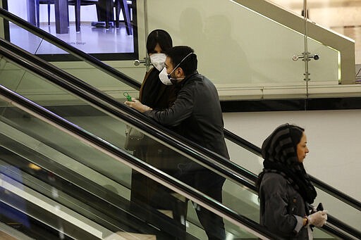 People wearing face masks and gloves ride an escalator at the Palladium Shopping Center, in northern Tehran, Iran, Tuesday, March 3, 2020. Iran's supreme leader put the Islamic Republic's armed forces on alert Tuesday to assist health officials in combating the outbreak of the new coronavirus, the deadliest outside of China. (AP Photo/Vahid Salemi)