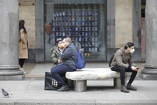 FILE - In this Thursday, Feb. 27, 2020, file photo, people wearing face masks sits on a bench in Milan, Italy. Health officials say passengers who flew on a jet with a Georgia man who later tested positive for the COVID-19 virus were never screened based on guidance from the Centers for Disease Control and Prevention. At a Tuesday, March 3, 2020, news briefing, local health officials said the 56-year-old Fulton County man had traveled to Atlanta from Milan, Italy, on Feb. 22 and didn&#146;t show symptoms of the disease until a few days after his flight. (AP Photo/Luca Bruno, File)