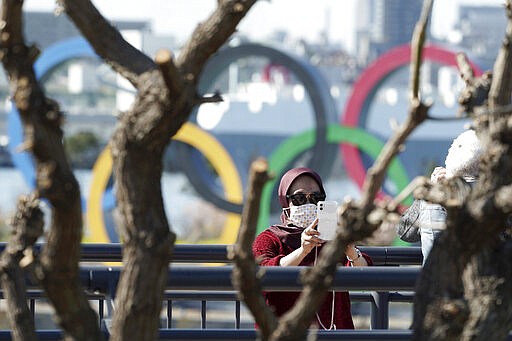 A tourist wearing a protective mask takes a photo with the Olympic rings in the background Tuesday, March 3, 2020, at Tokyo's Odaiba district. The spreading virus from China has put the Tokyo Olympics at risk. The Olympics are to open on July 24 - less than five months away. (AP Photo/Eugene Hoshiko)