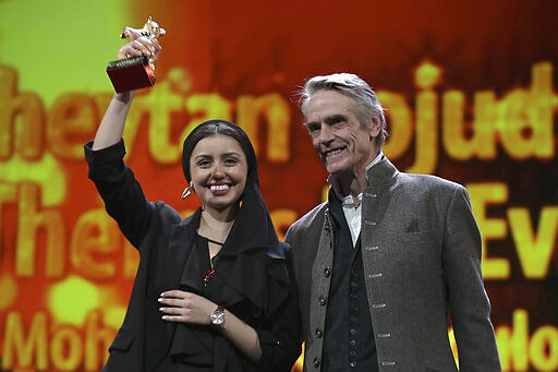 Actress Baran Rasoulof, left, holds aloft The Golden Bear for Best Film in place of director Mohammad Rasoulof, who did not attend, for the film 'Sheytan vojud nadarad' (There Is No Evil), presented by actor Jeremy Irons during the award ceremony at the 70th International Berlinale Film Festival in Berlin, Germany. Saturday, Feb. 29, 2020. (AP Photo/Michael Sohn)