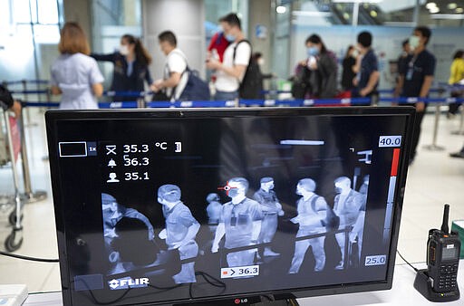 Tourists walk in front of a thermal scanner to check body temperatures as they arrive at the Suvarnabhumi Airport in Bangkok, Thailand, Wednesday, March 4, 2020. (AP Photo/Sakchai Lalit)